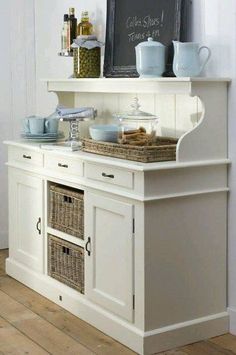 a kitchen with white cabinets and baskets on the top shelf, next to a chalkboard