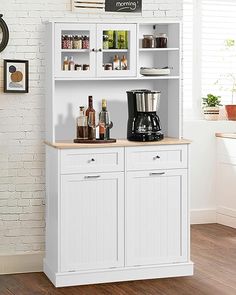 a white kitchen cabinet with two coffee makers on the top and shelves above it, in front of a brick wall