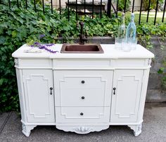 a sink sitting on top of a white cabinet next to a fence and green plants