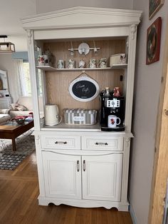 a white hutch with coffee maker and cups on it's shelves in a living room